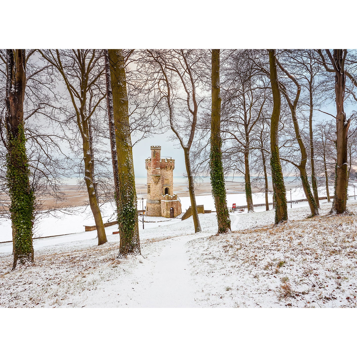 Appley Tower by Available Light Photography captures the cold beauty of a small stone tower standing solitary among leafless trees on a snowy landscape. The serene paths weaving through the snow invite exploration of this enigmatic scene.