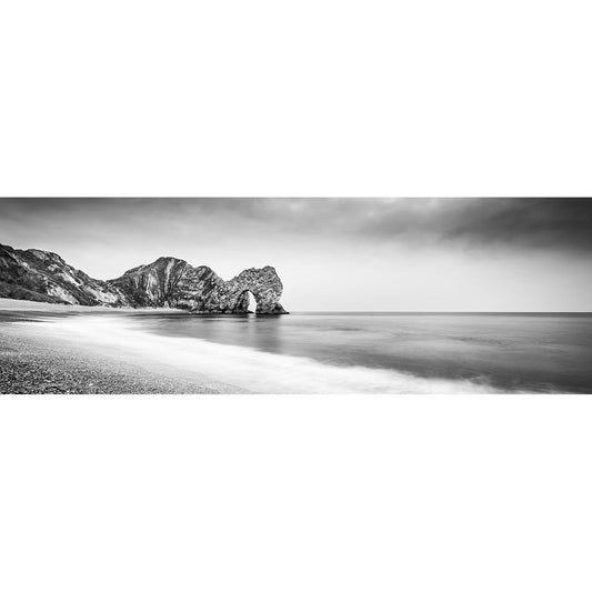 A black-and-white long exposure photograph of Durdle Door, a serene beach with smooth water and a rocky outcrop with an arch on the Isle of Wight by Available Light Photography.
