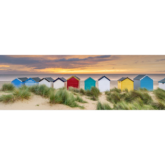 Row of colorful beach huts on a sandy shore at sunset in Southwold, captured by Available Light Photography.
