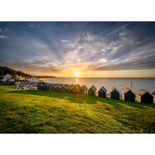 Sunrise over a serene beach with colorful Gurnard huts and a calm sea on Wight by Available Light Photography.