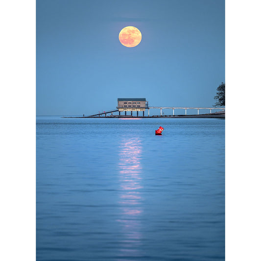A Moonrise from Bembridge Lifeboat Station hovers over a serene seascape with a pier and a solitary figure in a red kayak off the Isle of Wight, captured by Available Light Photography.