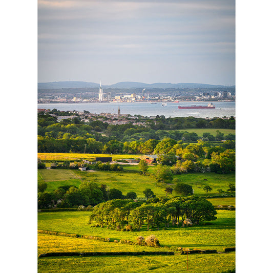 Lush green foreground with scattered trees leading to a cityscape and industrial harbor in the distance, under a cloudy sky on the Isle of Wight. - View from Ashey Down by Available Light Photography