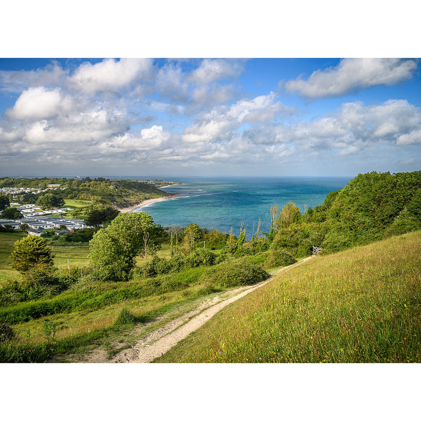 A scenic coastal landscape on the Isle with a path leading towards Whitecliff Bay, under a partly cloudy sky by Available Light Photography.