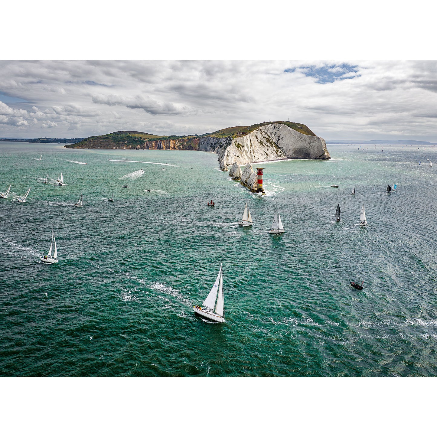 Sailboats racing near the Isle of Wight's coastal headland with a lighthouse during the Round the Island Race 2023 captured by Available Light Photography.