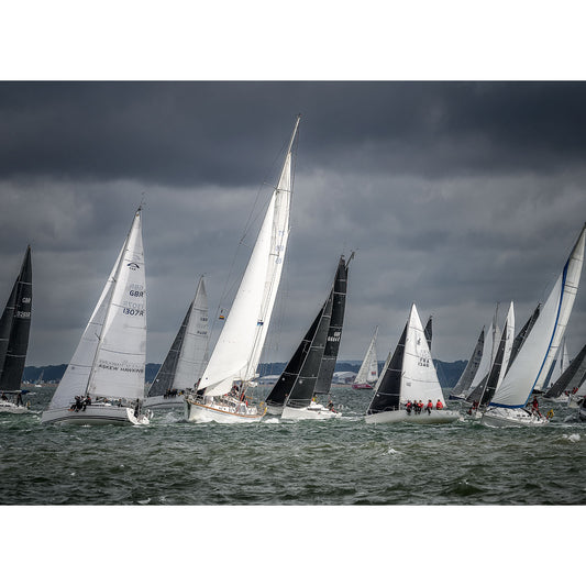 A fleet of sailboats, including one skippered by Steve Gascoigne, racing in the Round the Island Race on choppy waters off the Isle of Wight under a cloudy sky captured by Available Light Photography.