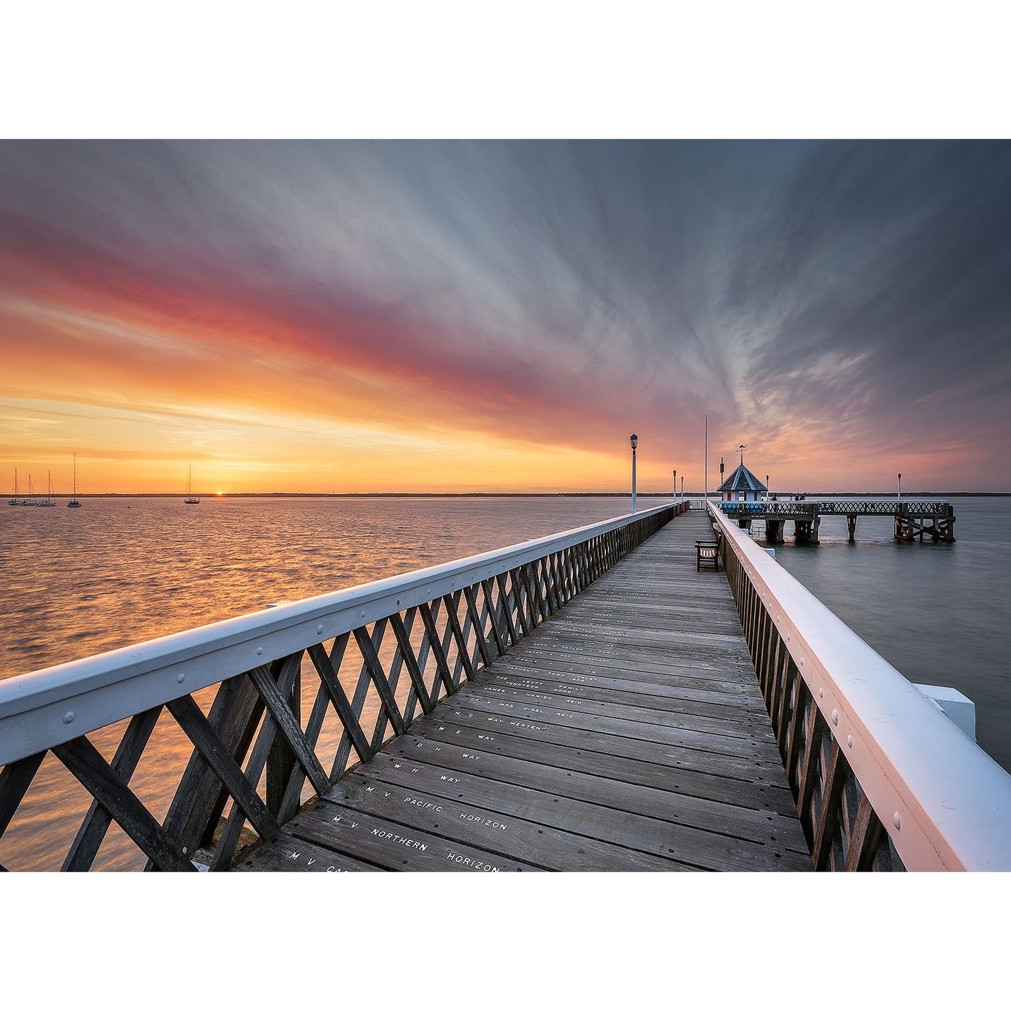 Wooden Yarmouth Pier extending into the ocean with a colorful sunset sky on Wight by Available Light Photography.