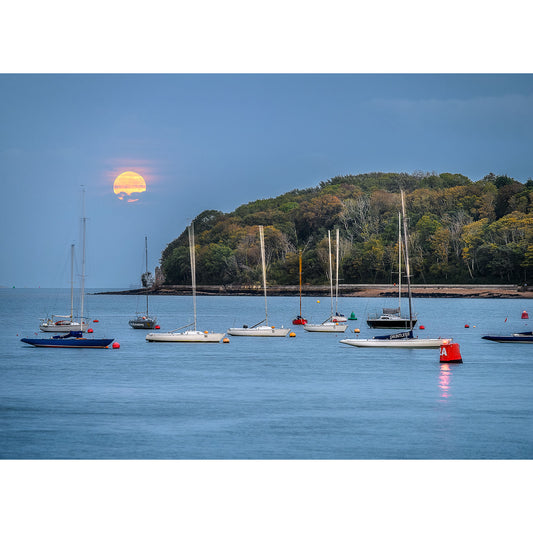 Sailboats moored in tranquil waters at dusk near Wight with Moonrise over East Cowes, a product by Available Light Photography, partially obscured sun setting near the horizon.