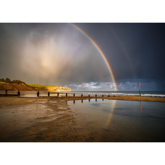 A double Rainbow over Culver Cliff arcs over the serene Isle of Wight beach with reflective wet sand under a dramatic sky. (Available Light Photography)