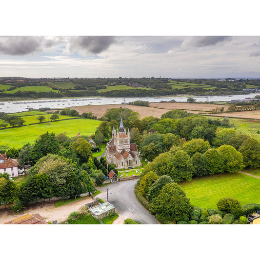 Image 2808: Aerial view of St Mildred's Church, Whippingham surrounded by lush greenery with a river and overcast skies in the background. (Available Light Photography)