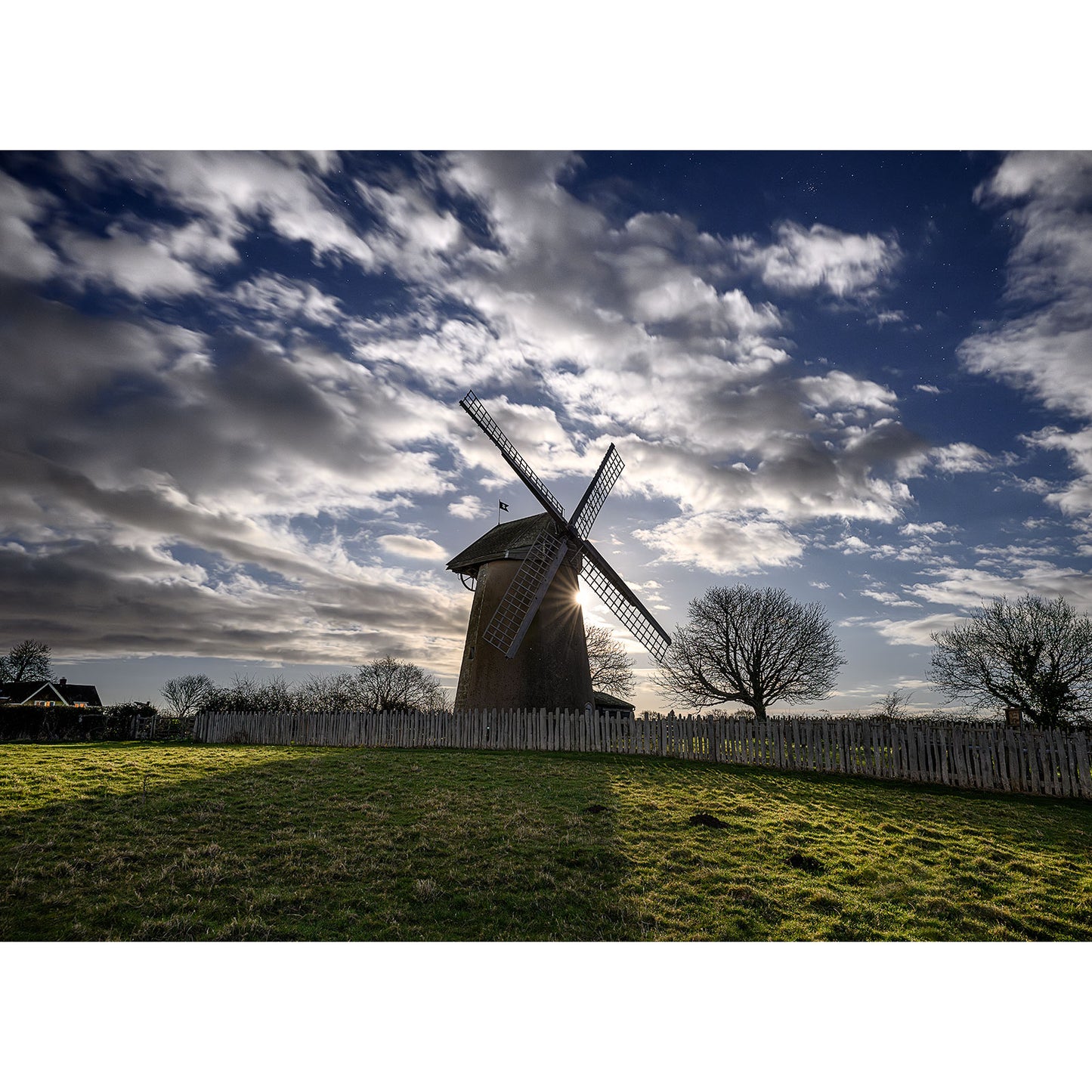 A Bembridge Windmill stands against a dramatic night sky, with Moonlit clouds breaking through, captured by Available Light Photography.