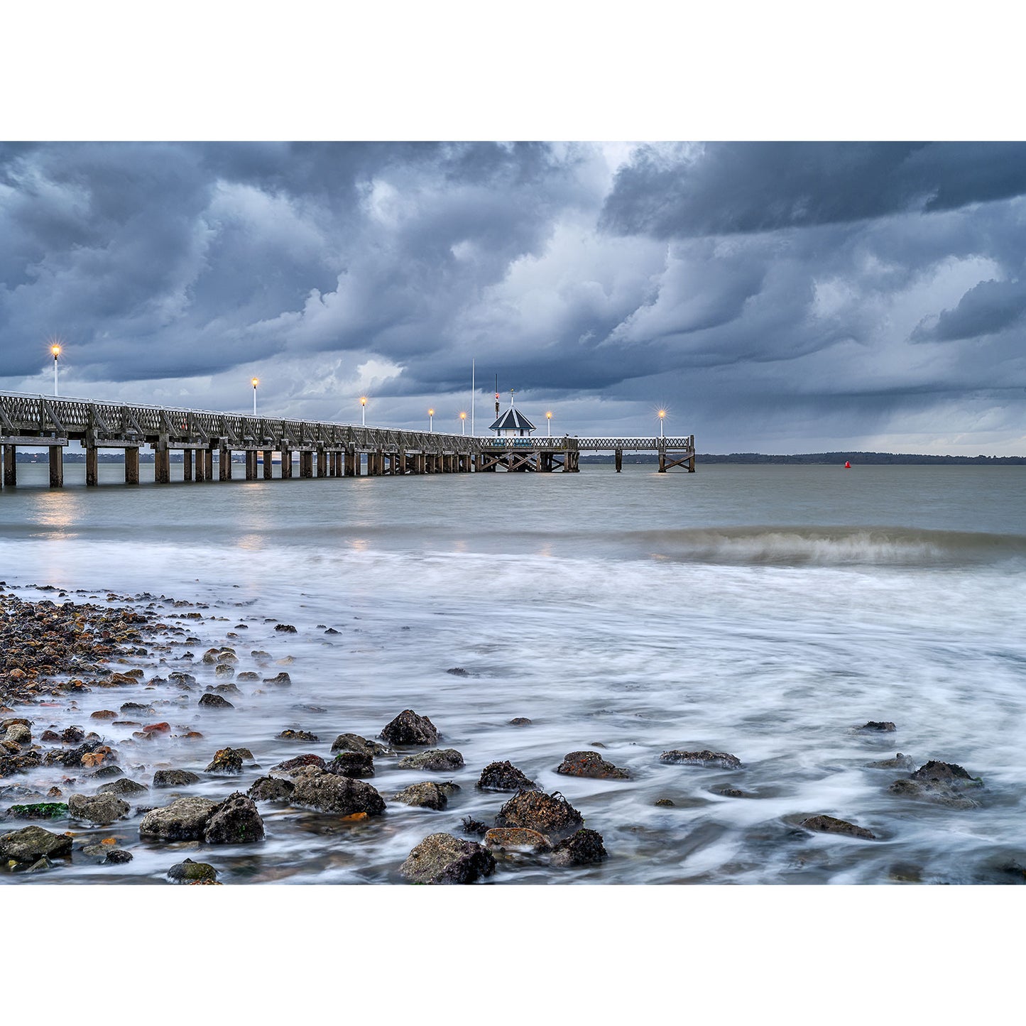Yarmouth Pier extending into the sea with cloudy skies at twilight and smooth water effect on the shoreline by Available Light Photography.