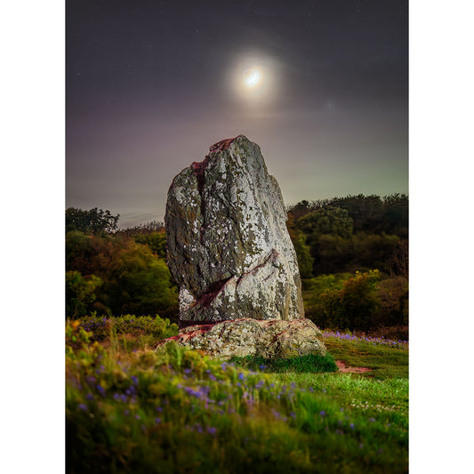A large, weathered Longstone titled "The Longstone" by Available Light Photography is illuminated by moonlight in a grassy field with scattered purple flowers, surrounded by trees and an ethereal display of the northern lights in the background.