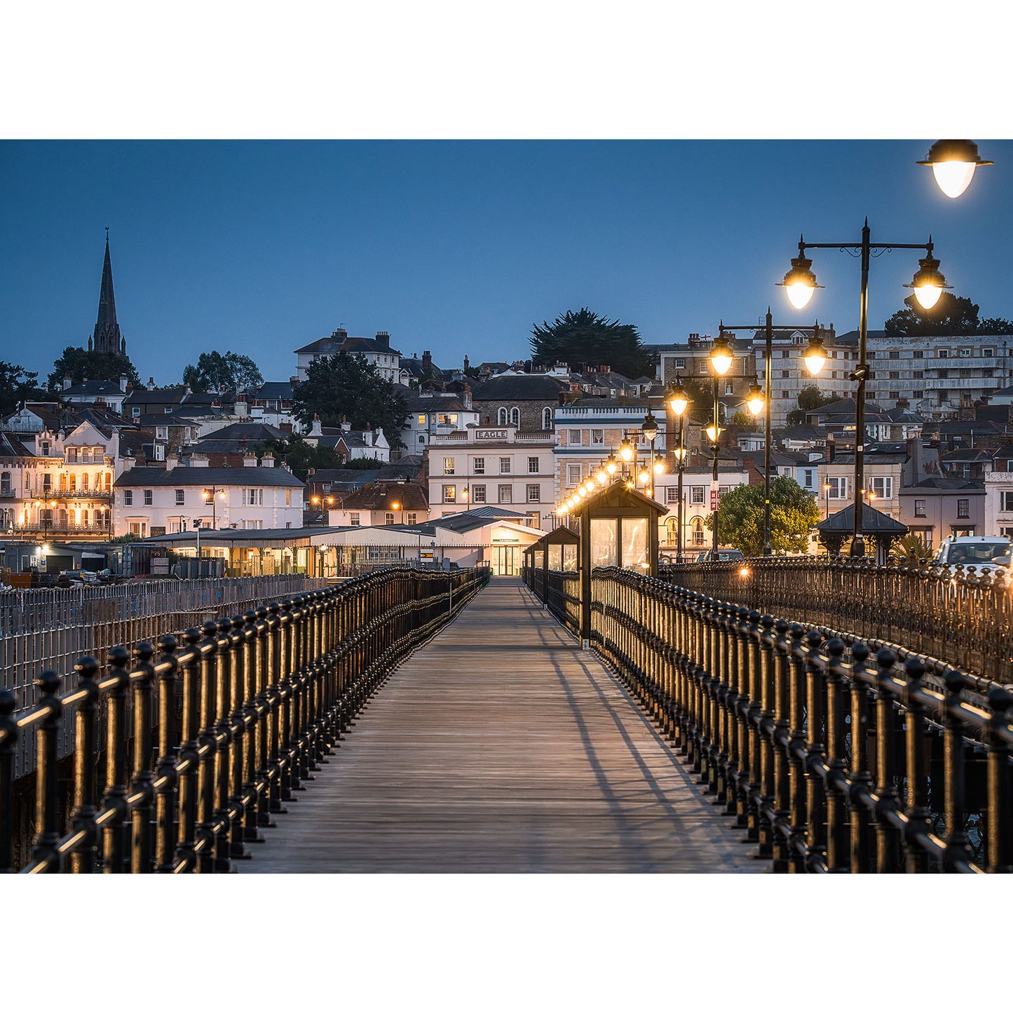 Ryde Pier, captured in an air of mystery by Available Light Photography, draws you toward a quaint town with buildings gently illuminated at dusk.