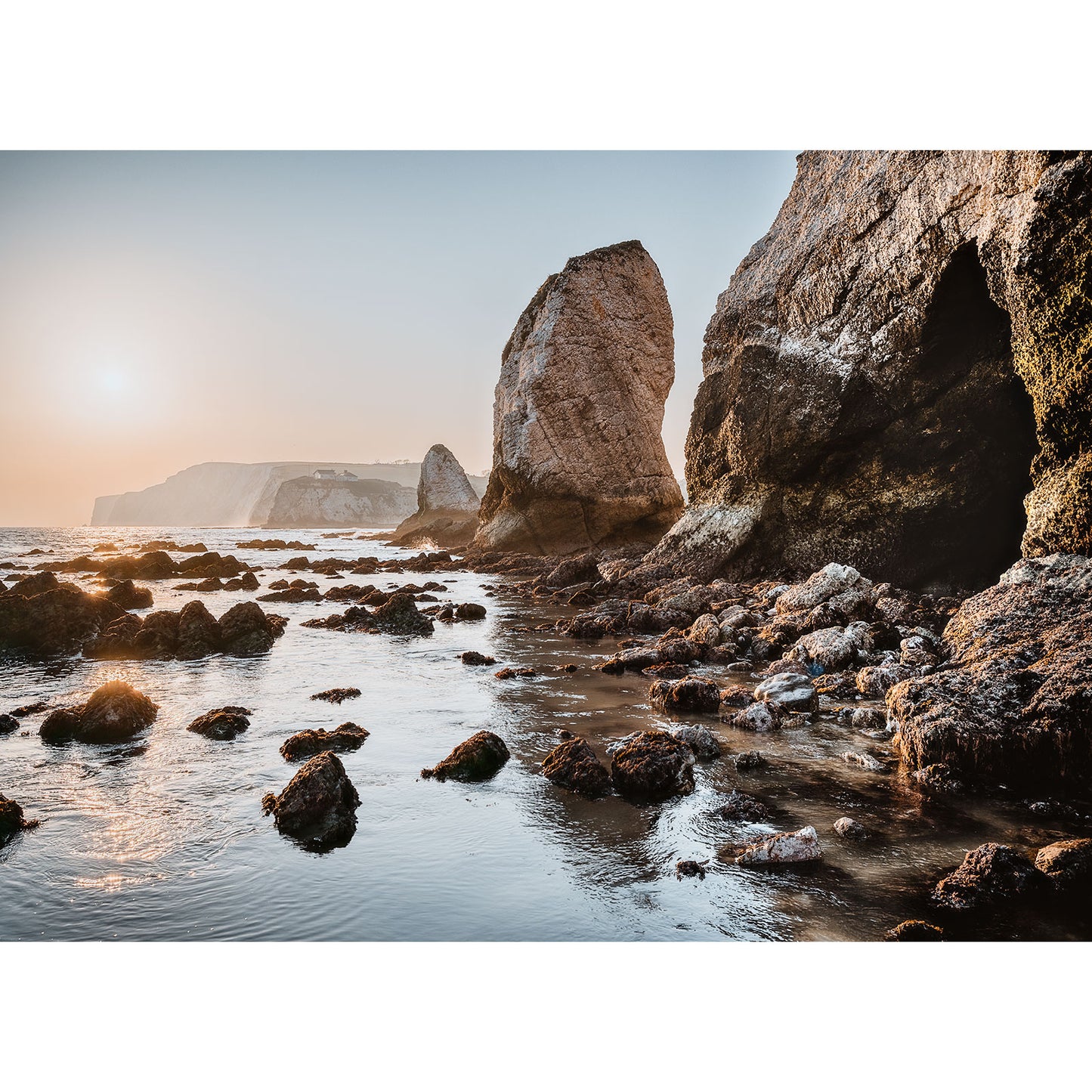 At sunrise, the rocky shoreline of Freshwater Bay reveals stunning large rock formations as a distant cliff stands proud under a clear sky. No product description is provided to identify SEO keywords here, but this piece by Available Light Photography captures nature's serene beauty.