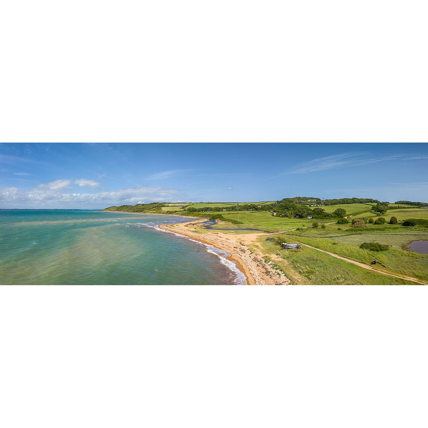 Thorness Bay by Available Light Photography captures a serene coastal landscape with a sandy beach, green fields, scattered trees, and a blue sky—perfect for relaxation.