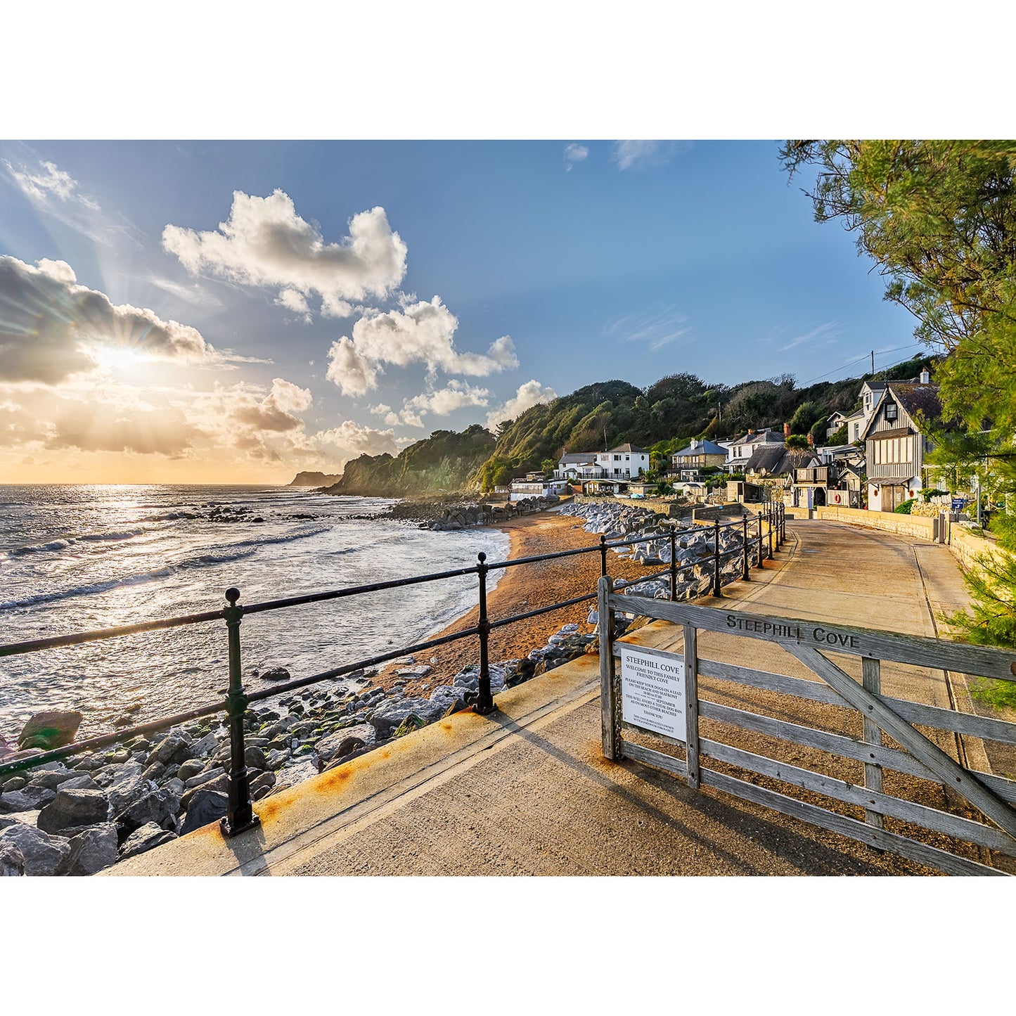 Steephill Cove by Available Light Photography captures a gated view of the cove’s rocky beach, seaside cottages, rolling hills, and gentle waves under a partly cloudy sunset sky.