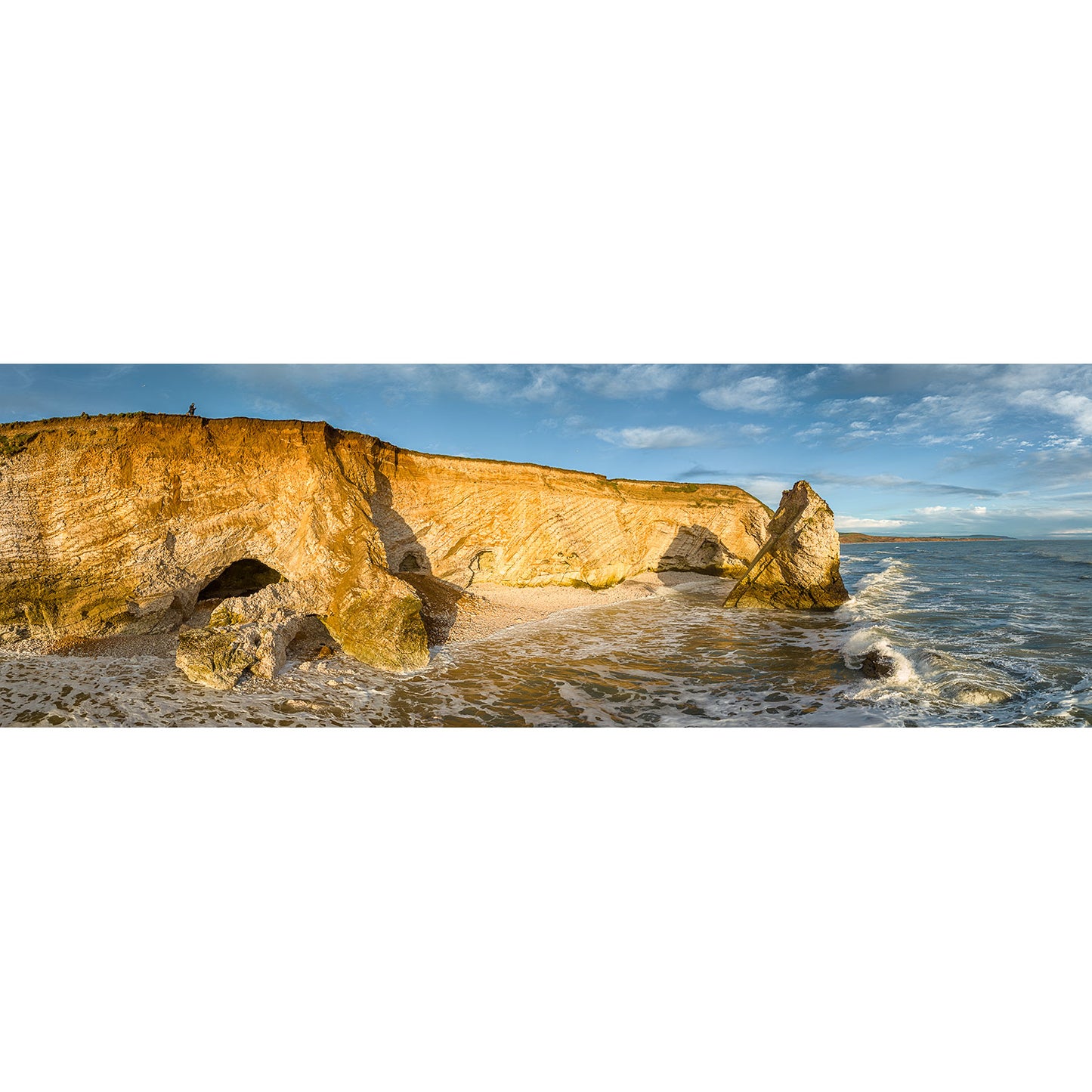 Freshwater Bay by Available Light Photography captures rugged golden sea cliffs, rocky formations, and waves washing onto sandy shores beneath a blue sky with scattered clouds—a stunning coastal scene.