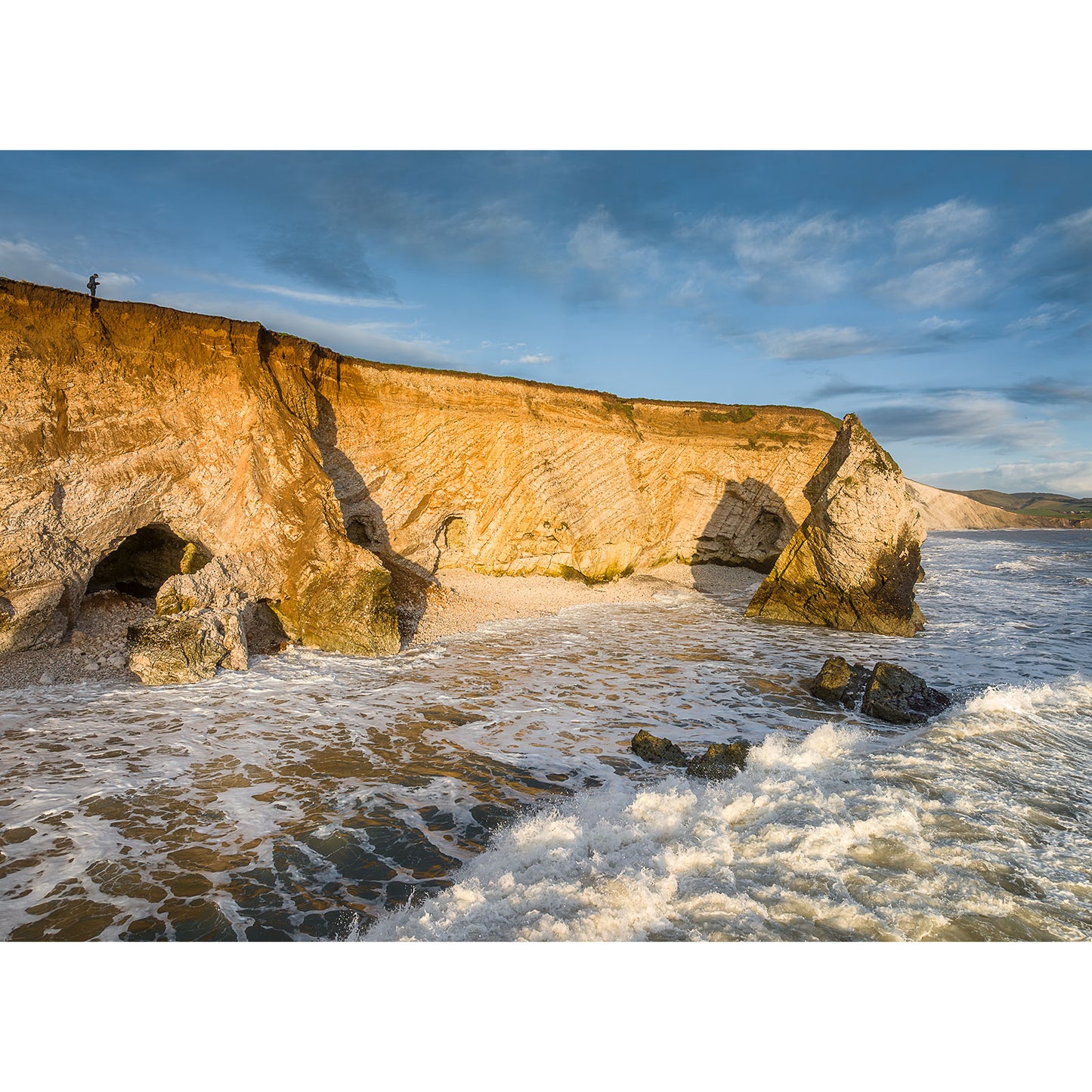 Freshwater Bay by Available Light Photography captures coastal cliffs, dramatic sea caves, and striking rock formations along the shore as waves crash beneath a clear blue sky.