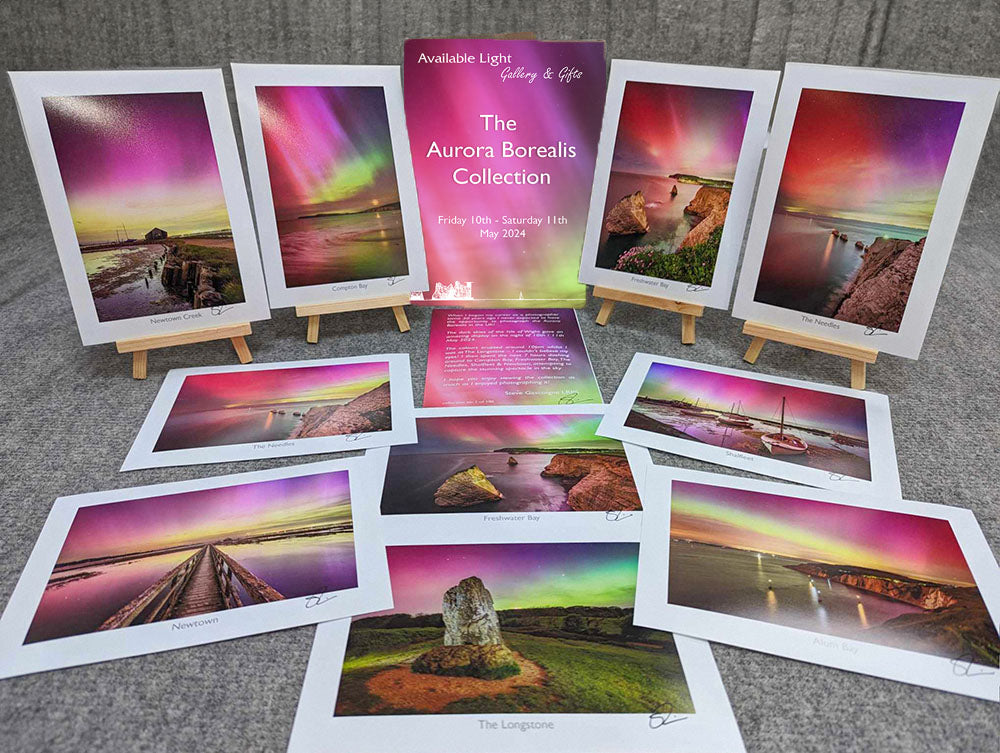 A display of nine framed photos showcasing Northern Lights scenes, arranged around a poster titled "The Aurora Borealis Collection" by Available Light Photography, detailing an event from May 10th to 11th, 2014. These limited edition prints capture the mesmerizing beauty seen from the Isle of Wight.
