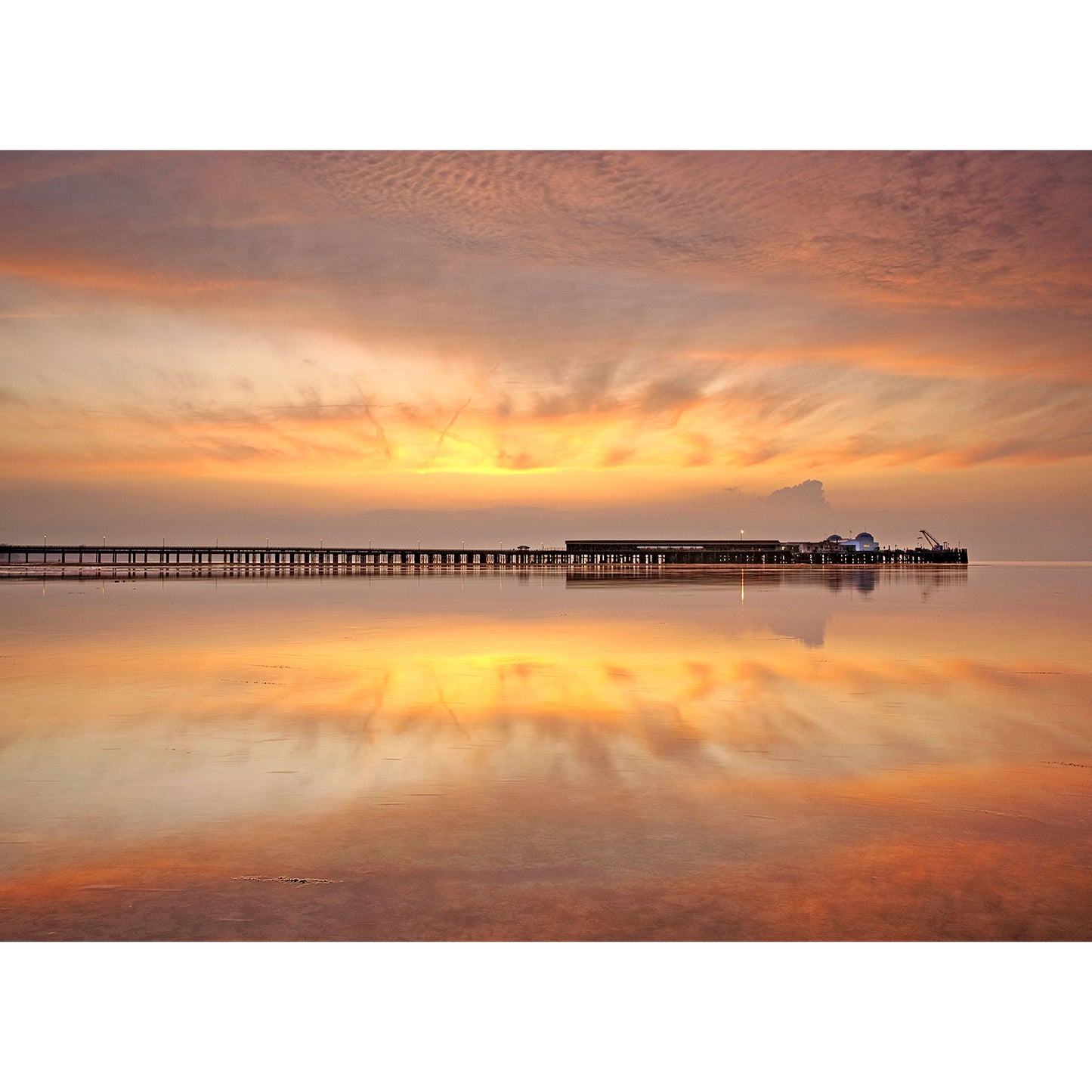 A serene sunset with vivid colors reflecting off calm water at the Isle of Wight, featuring Ryde Pier extending into the sea, captured by Available Light Photography.