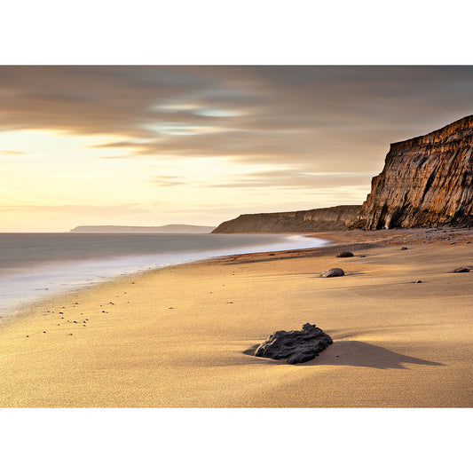 Serene beach at sunset with cliffs in the distance and a rock in the foreground on the Isle of Wight captured beautifully by Chale Bay from Available Light Photography.