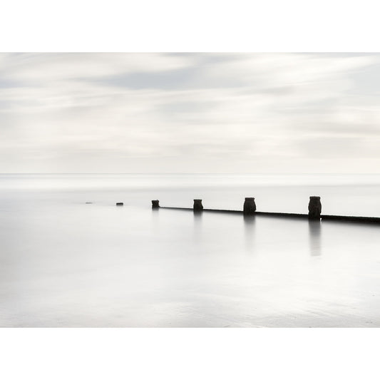 A serene seascape with a line of breakwater posts disappearing into the calm, misty horizon off the Isle of Wight captured by Shades of White, Sandown Bay by Available Light Photography.