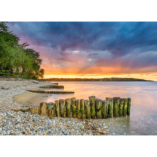 Sunset over Bembridge Beach on the Isle of Wight with wooden pilings and a dramatic clouded sky captured by Available Light Photography.