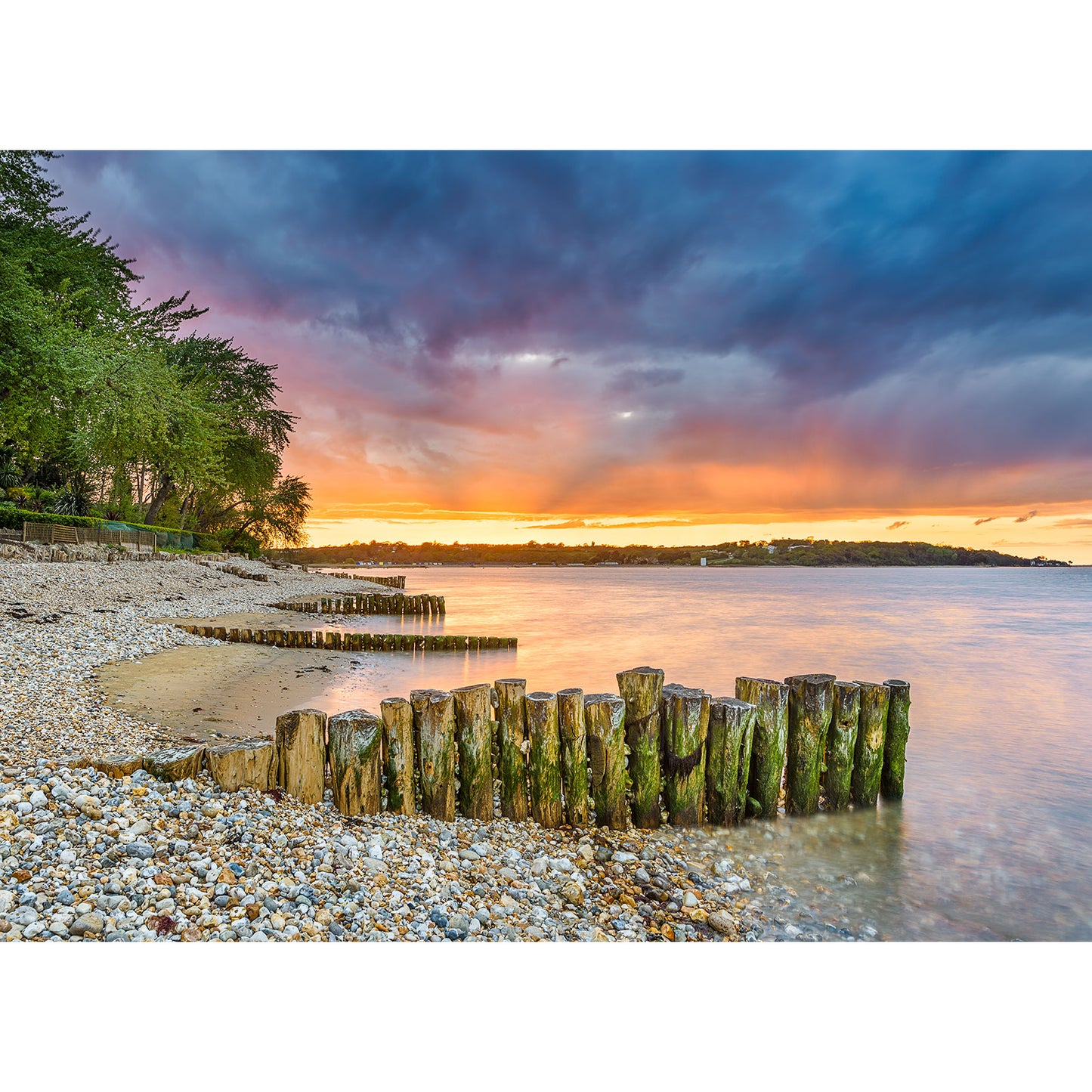 Sunset over Bembridge Beach on the Isle of Wight with wooden pilings and a dramatic clouded sky captured by Available Light Photography.