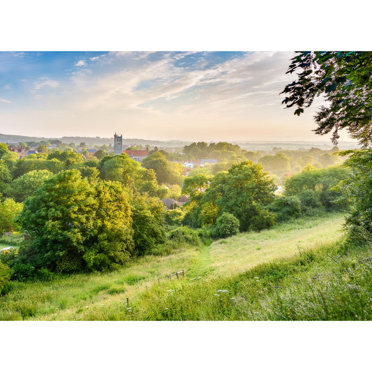 A serene sunrise over a lush, green countryside with a village and church tower peaking through the foliage on the Isle of Wight captured in "Carisbrooke" by Available Light Photography.