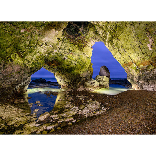 A cavernous rocky archway on the Isle opens up to a serene beach and calm sea at dusk in the caves at Freshwater Bay by Available Light Photography.