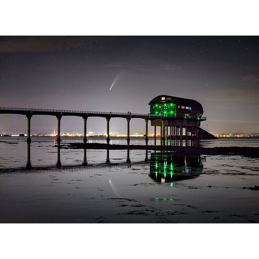 A pier on the Isle of Wight with illuminated green lights at night, reflecting on the water's surface with Comet Neowise visible in the starry sky. Photography by Available Light Photography at Bembridge Lifeboat Station.