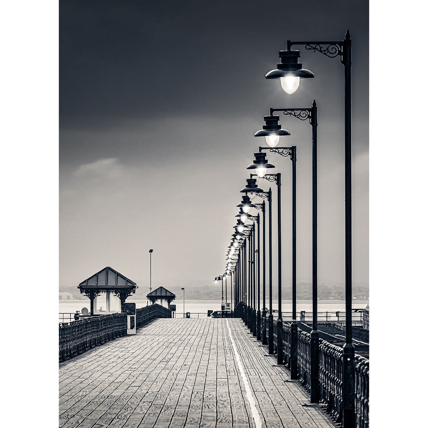 A row of Ryde Pier lamp posts lining a pier leading to a gazebo overlooking the water on Wight by Available Light Photography.