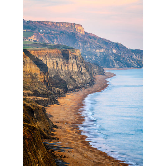 Cliff-lined coast at sunset with waves gently lapping onto the deserted beach.