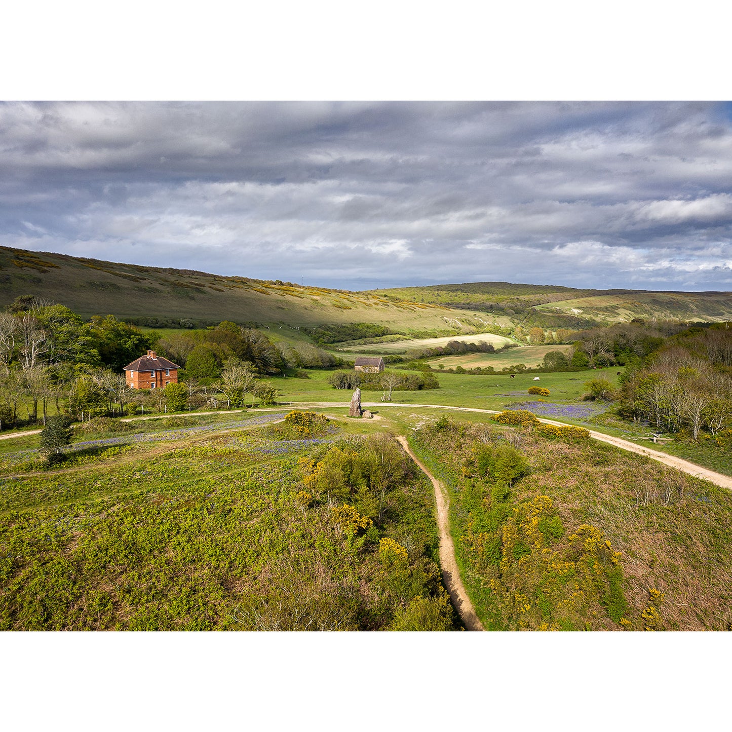 Pastoral landscape with a winding path leading to a Longstone house amidst lush greenery under a cloudy sky captured by Available Light Photography.