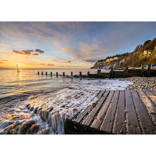 Sunset at Shanklin Beach with waves lapping against a wooden groyn and a view of chalk cliffs in the distance on the Isle of Wight by Available Light Photography.