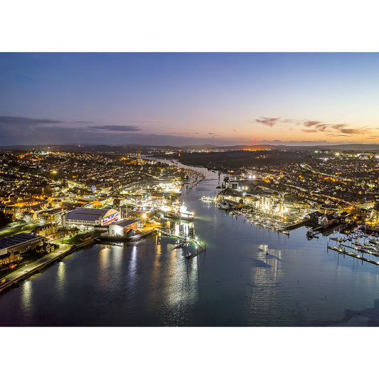 Aerial view of Cowes and East Cowes coastal town on Wight at dusk with illuminated streets and docks, and a sunset in the background taken by Available Light Photography.