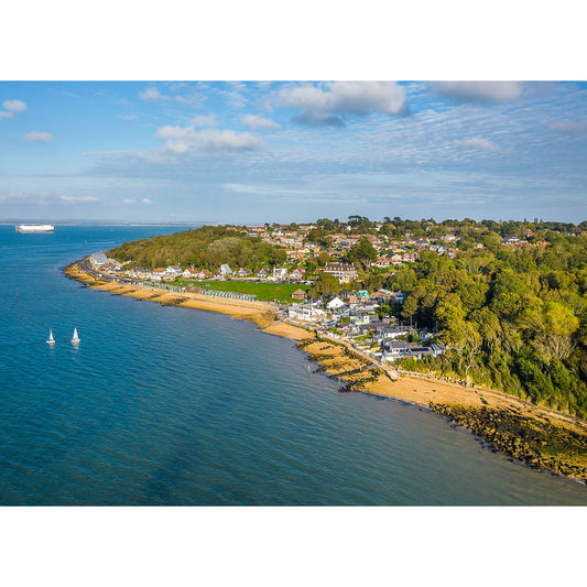 Aerial view of a Gurnard village with boats sailing near the shore and a clear blue sky overhead by Available Light Photography.