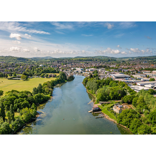 Aerial view of Newport town with a river flowing through, surrounded by greenery and hills under a blue sky with scattered clouds on the Isle Gascoigne by Available Light Photography.