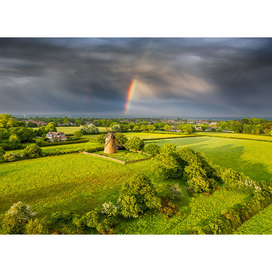 A partial rainbow emerges from a dramatic sky over a lush green rural landscape with the Bembridge Windmill monument photographed by Steve Gascoigne, captured by Available Light Photography.