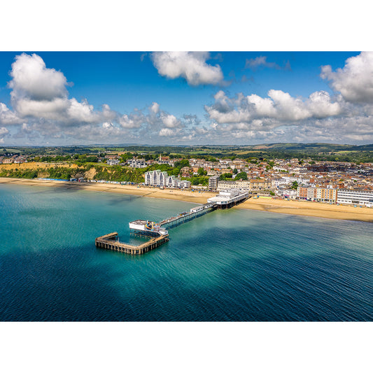 Aerial view of Sandown, a coastal town with a pier extending into the sea, sandy beach on one side, and urban buildings on the other. Photographed by Available Light Photography.