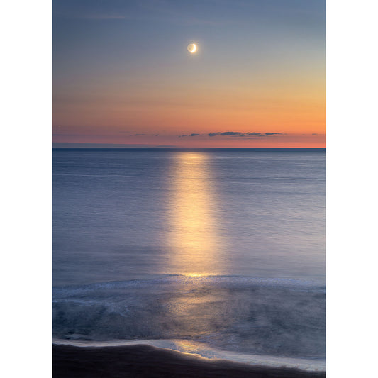 Crescent Moon over a tranquil sea with moonlight reflection on the water at dusk off the Isle of Wight, captured by Available Light Photography at Compton Bay.