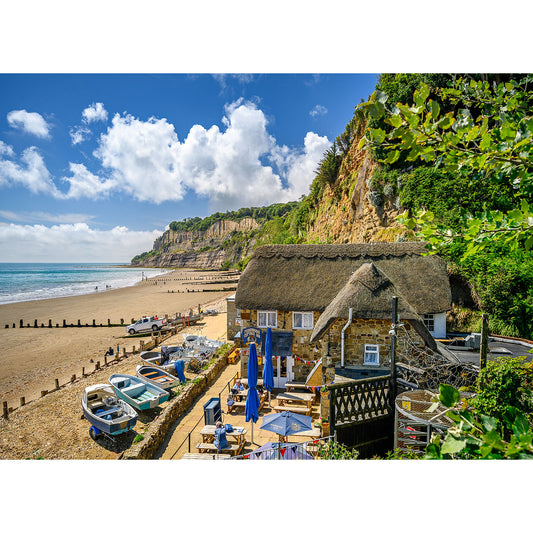 A Shanklin beach on the Isle of Wight with a thatched roof and boats on the beach by Available Light Photography.