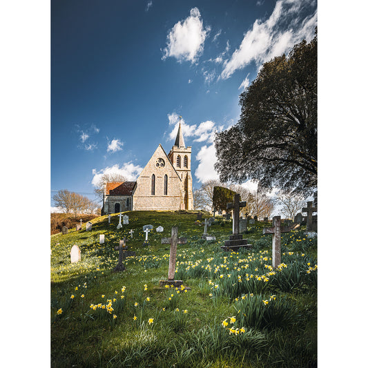 A quaint stone church with a spire overlooks a serene graveyard dotted with yellow flowers under a vibrant blue sky, capturing the tranquil essence of Church of Saint Mary, Brook by Available Light Photography.