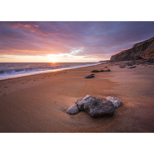 Sunset at a serene beach with rocks on the sand and cliffs in the distance by from Available Light Photography.