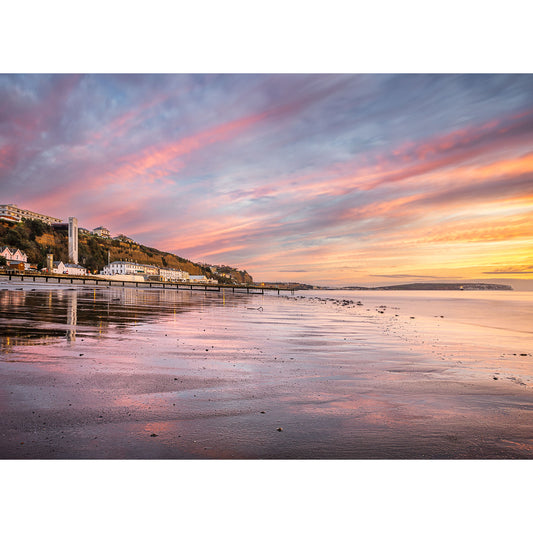 Shanklin Beach by Available Light Photography captures a coastal town at sunset with pastel clouds, calm water reflecting the sky, and buildings nestled along the shoreline against a gently sloping hillside.