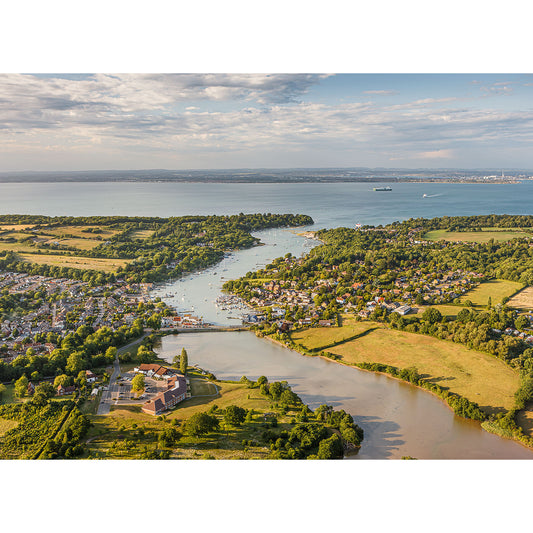 Aerial view of Wootton Creek by Available Light Photography, featuring a winding river through lush fields, houses, and boats, flowing into a larger body of water beneath a partly cloudy sky.