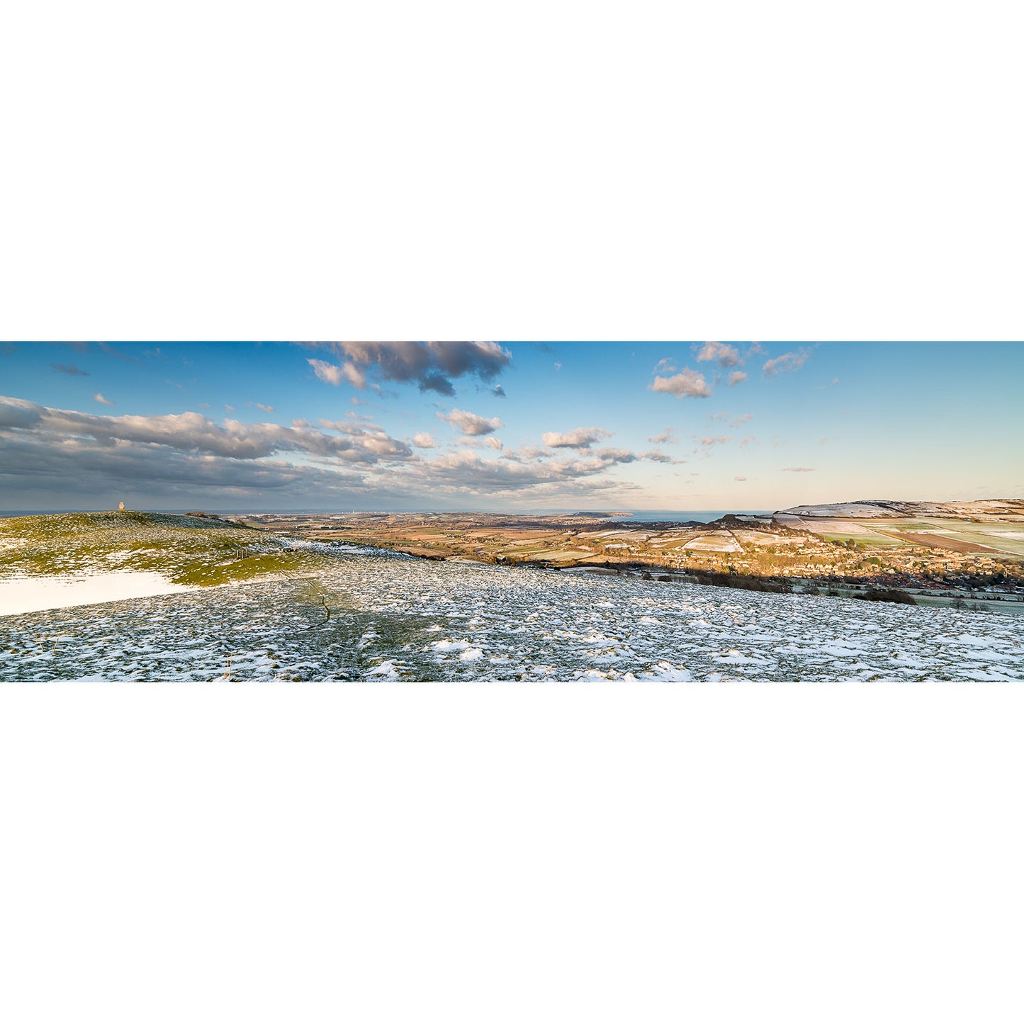 Wide panoramic view from Appuldurcombe Down: a frosty field with patches of snow beneath a blue sky and scattered clouds, distant hills on the horizon. Available Light Photography.