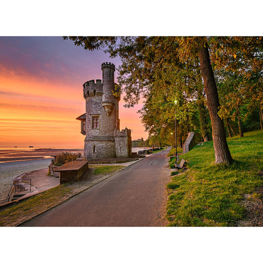 Appley Tower by Available Light Photography stands beside a paved path among trees and benches at sunset, overlooking a peaceful sandy beach and calm water.