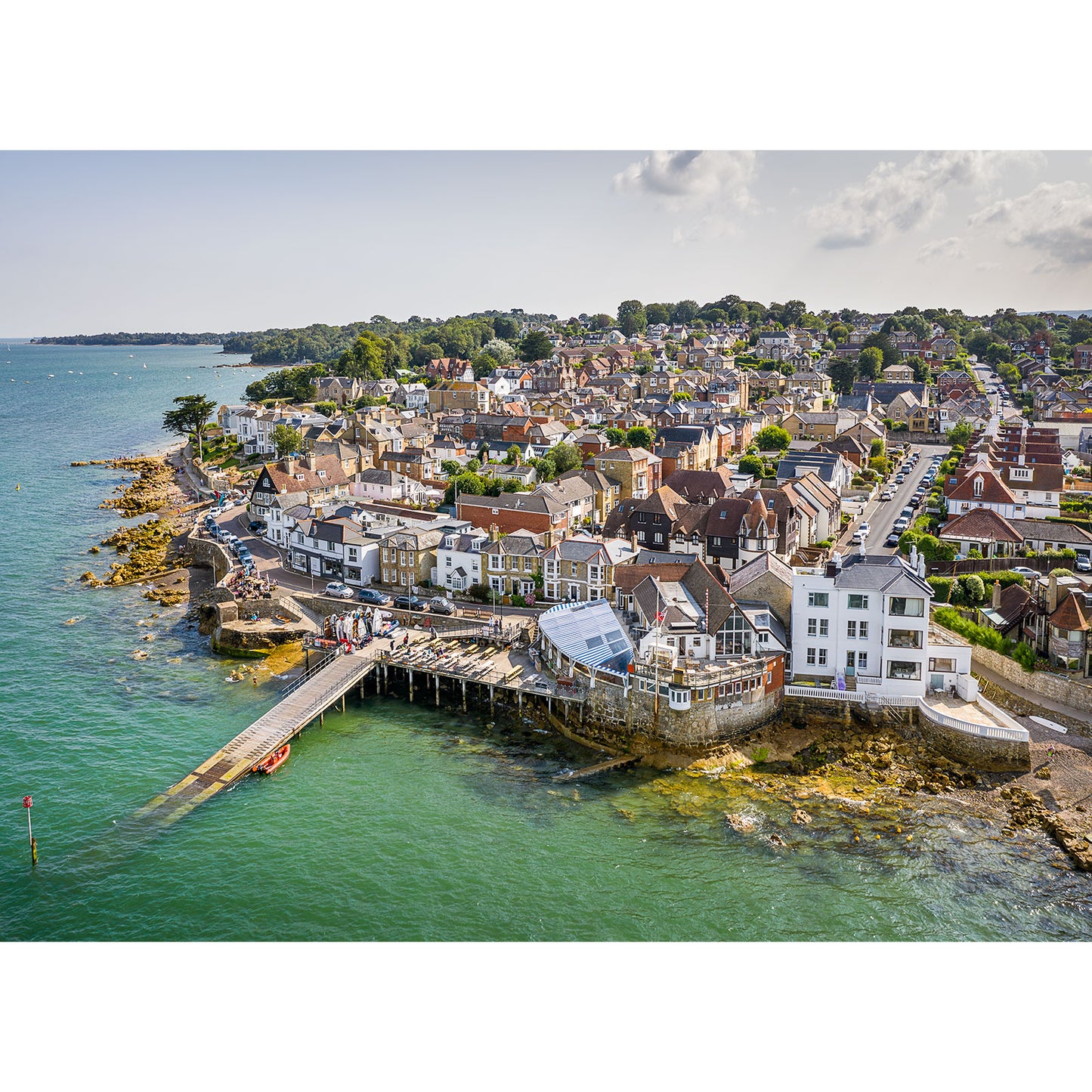 Aerial view of Seaview, a coastal town on the Isle of Wight with buildings adjacent to a pier extending into clear blue waters, captured by Available Light Photography.