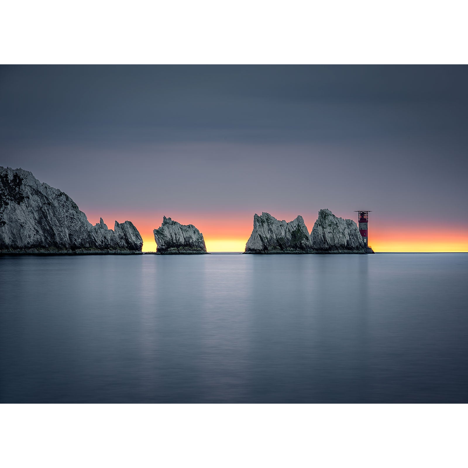 A serene seascape at dusk featuring rocky outcrops and a distant lighthouse on the Isle of Wight captured by The Needles from Available Light Photography.